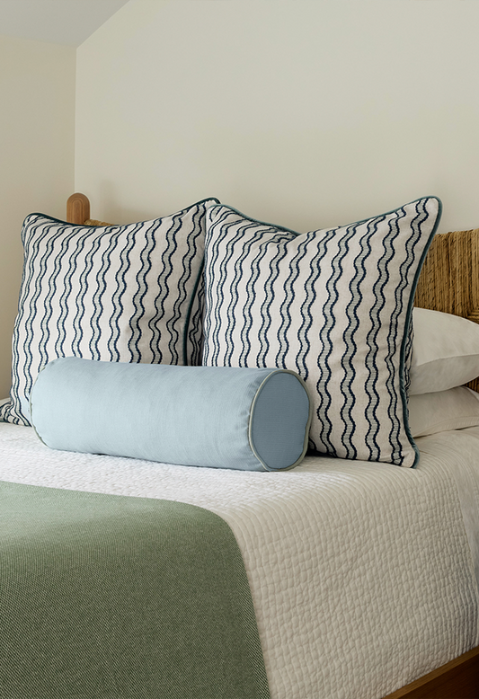 embroidered cream and navy blue wavy lines and light blue pillows on a bed with white and sage green bedding 
