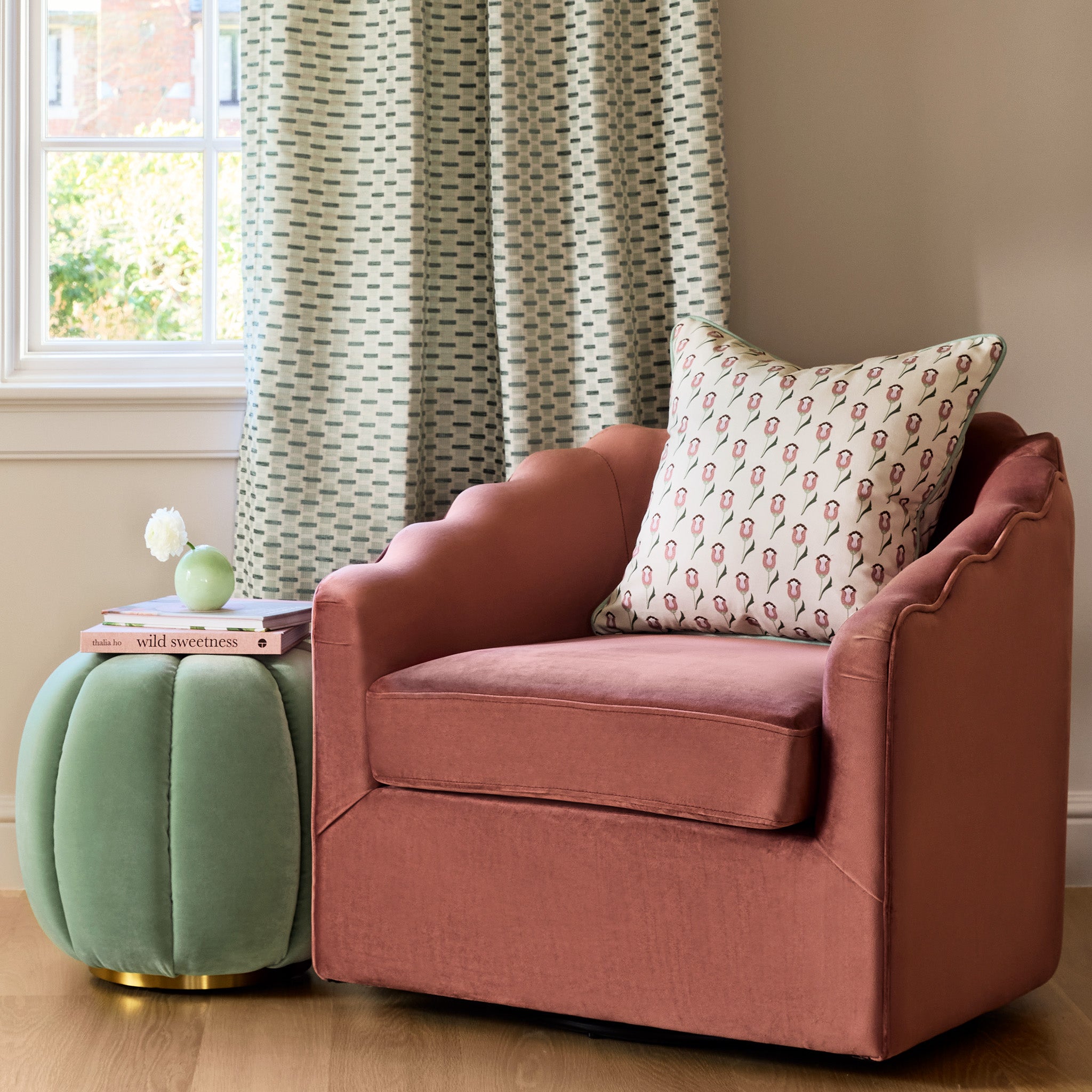  abstract floral pink and green printed pillow on a coral colored chair with a mint green ottoman stacked with books
