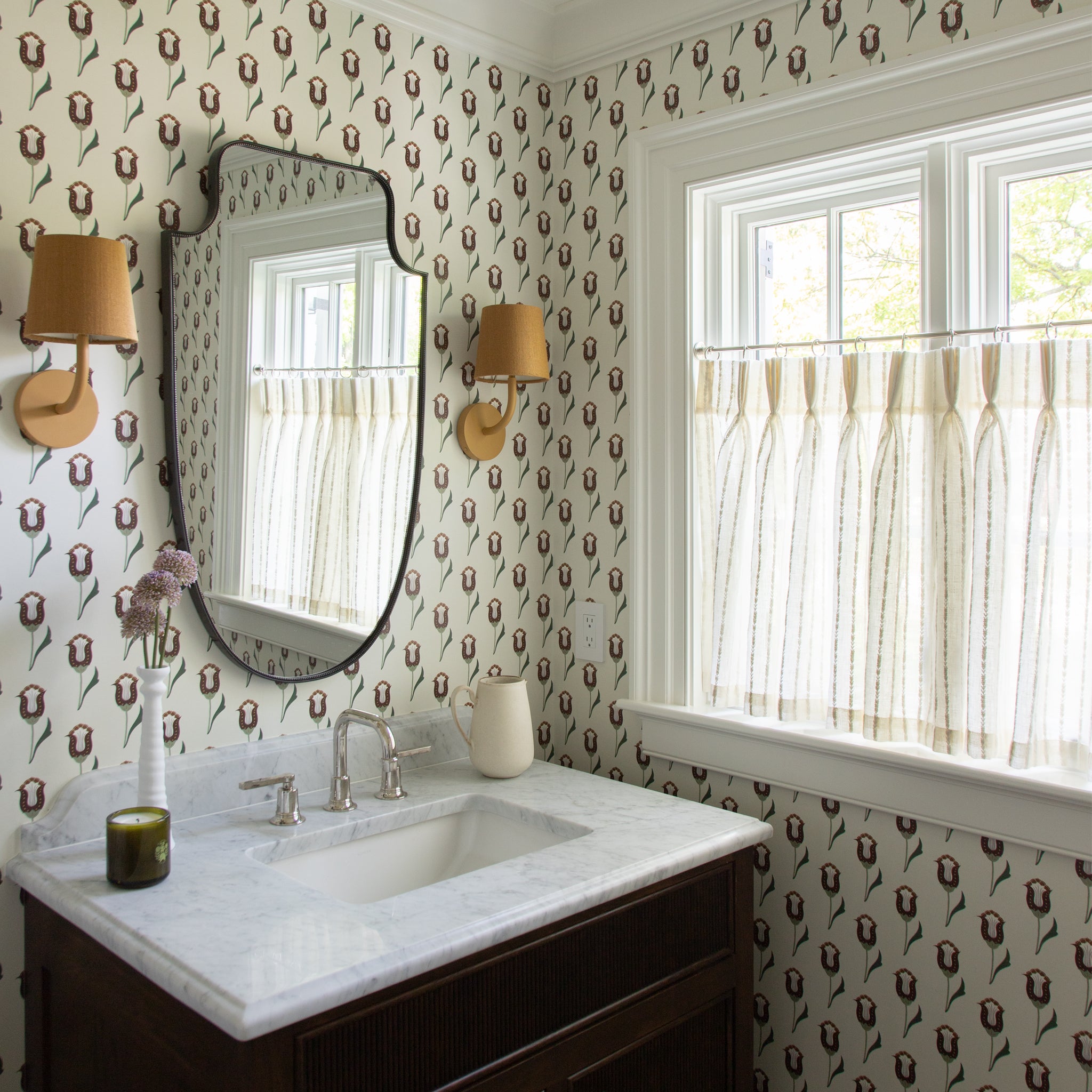 neutral background wallpaper with pink and maroon wallpaper in a bathroom with sheer white cafe curtains embroidered with white stripes hung in front of an illuminated window 