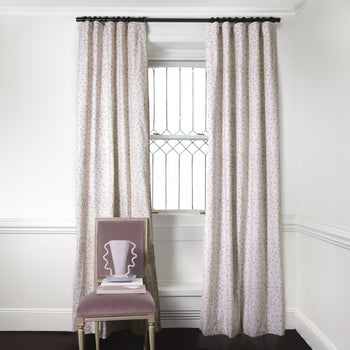 Beige Animal Print Curtains on metal rod in front of an illuminated window with Pink Velvet chair with pink vase on top of stacked books