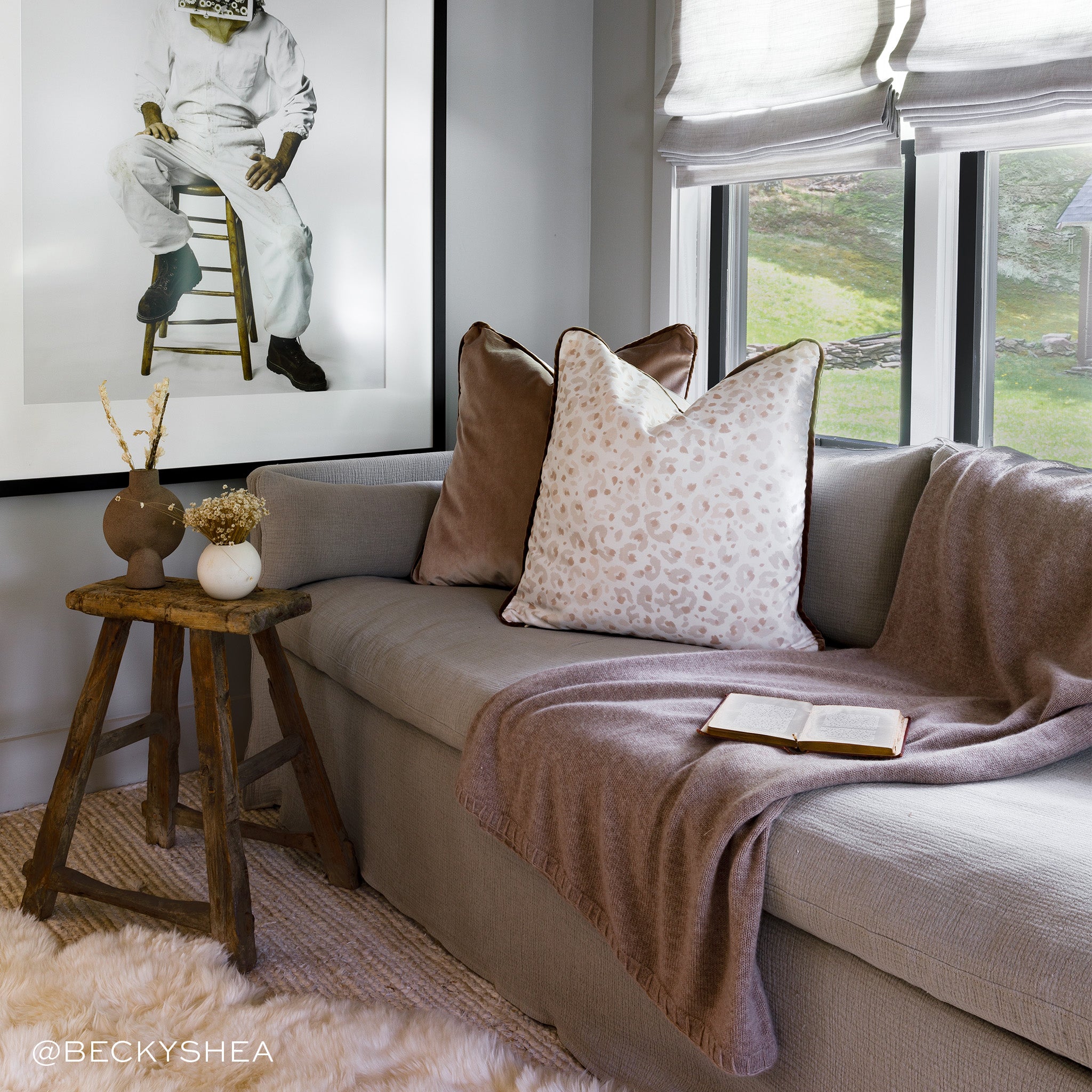 Room corner styled with brown velvet pillow and Beige Animal Print Pillow on brown couch next to wooden stool with two vases on top and framed artwork hung on wall. Photo taken by Becky Shea