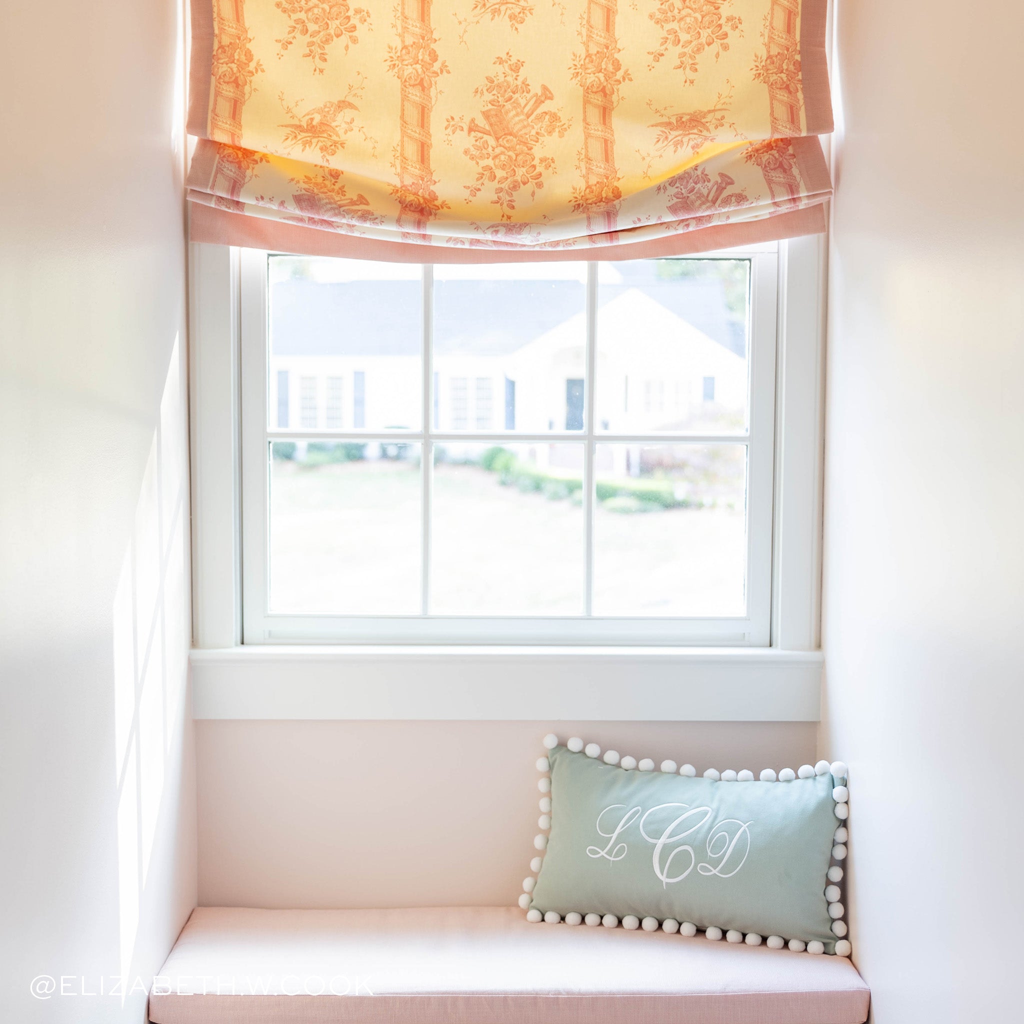 Corner illuminated window styled with sage green monogrammed pillow with white pom poms. Photo taken by Elizabeth W Cook
