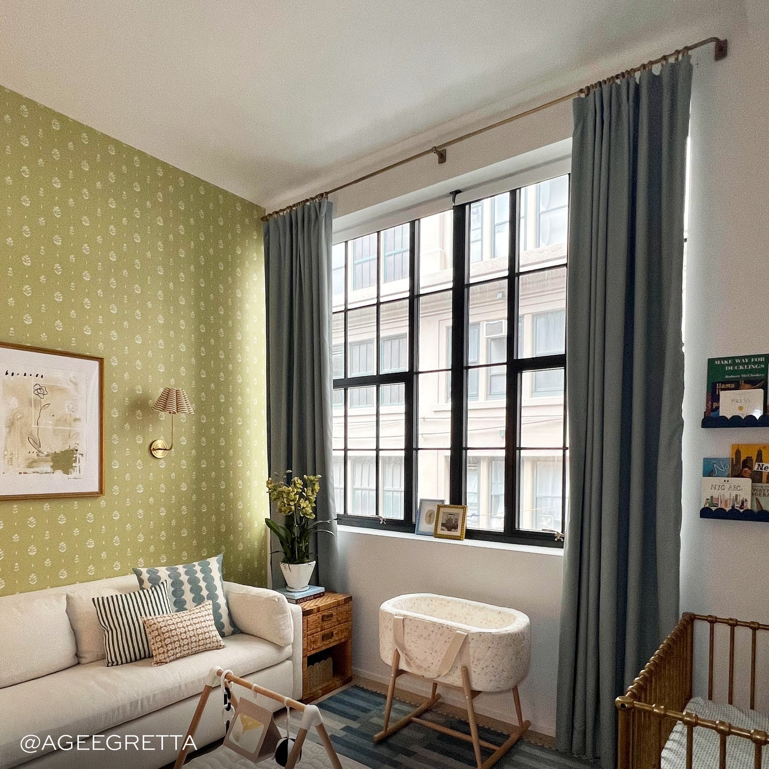 Grey blue curtains on a metal rod in front of an illuminated window with green wallpaper on the walls and a white couch