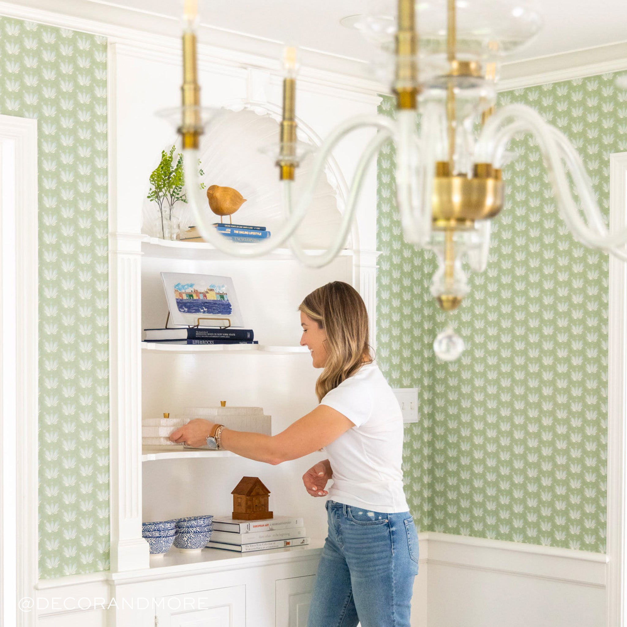 Dining room corner close-up styled with a Blue & Green Floral Drop Repeat Printed Wallpaper and white shelves with plates and decorations being held by blonde woman wearing white t-shirt and jeans