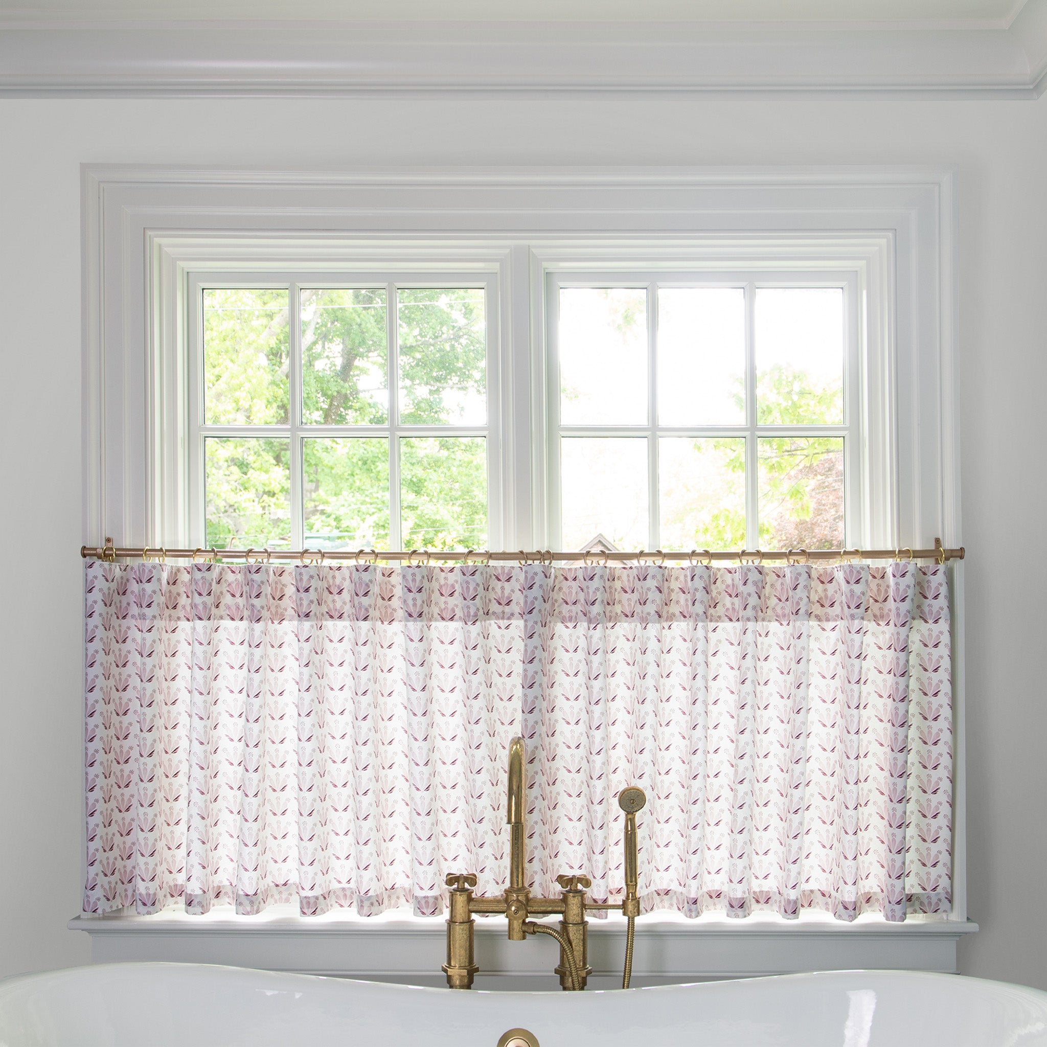 Pink & Burgundy Drop Repeat Floral  cafe curtain hung in front of an illuminated window in a bathroom with a white bathtub in front of the window with a gold faucet 