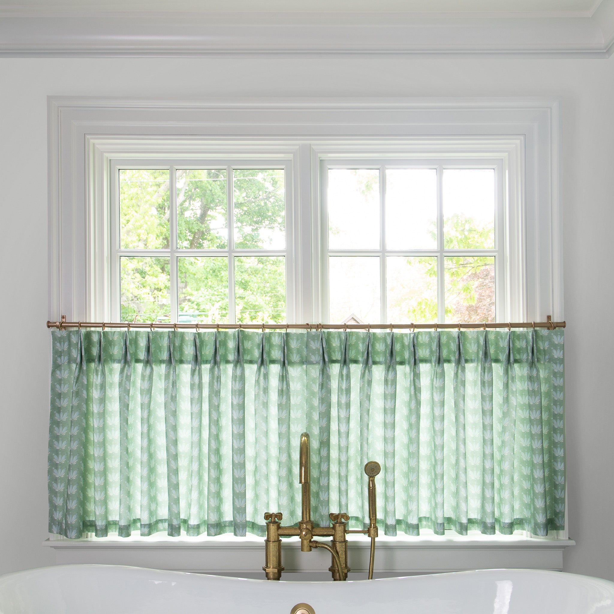 Blue & Green Floral Drop Repeat Printed Cotton curtain on a metal rod in front of an illuminated window in a bathroom 