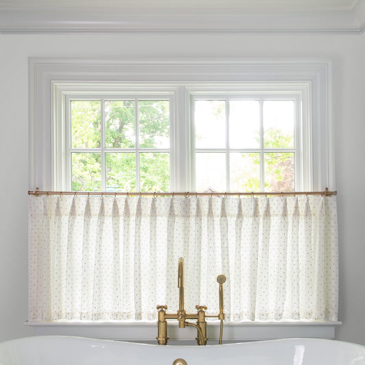 white sheer curtain with embroidered pink polka dots on a metal rod in front of an illuminated window in a bathroom
