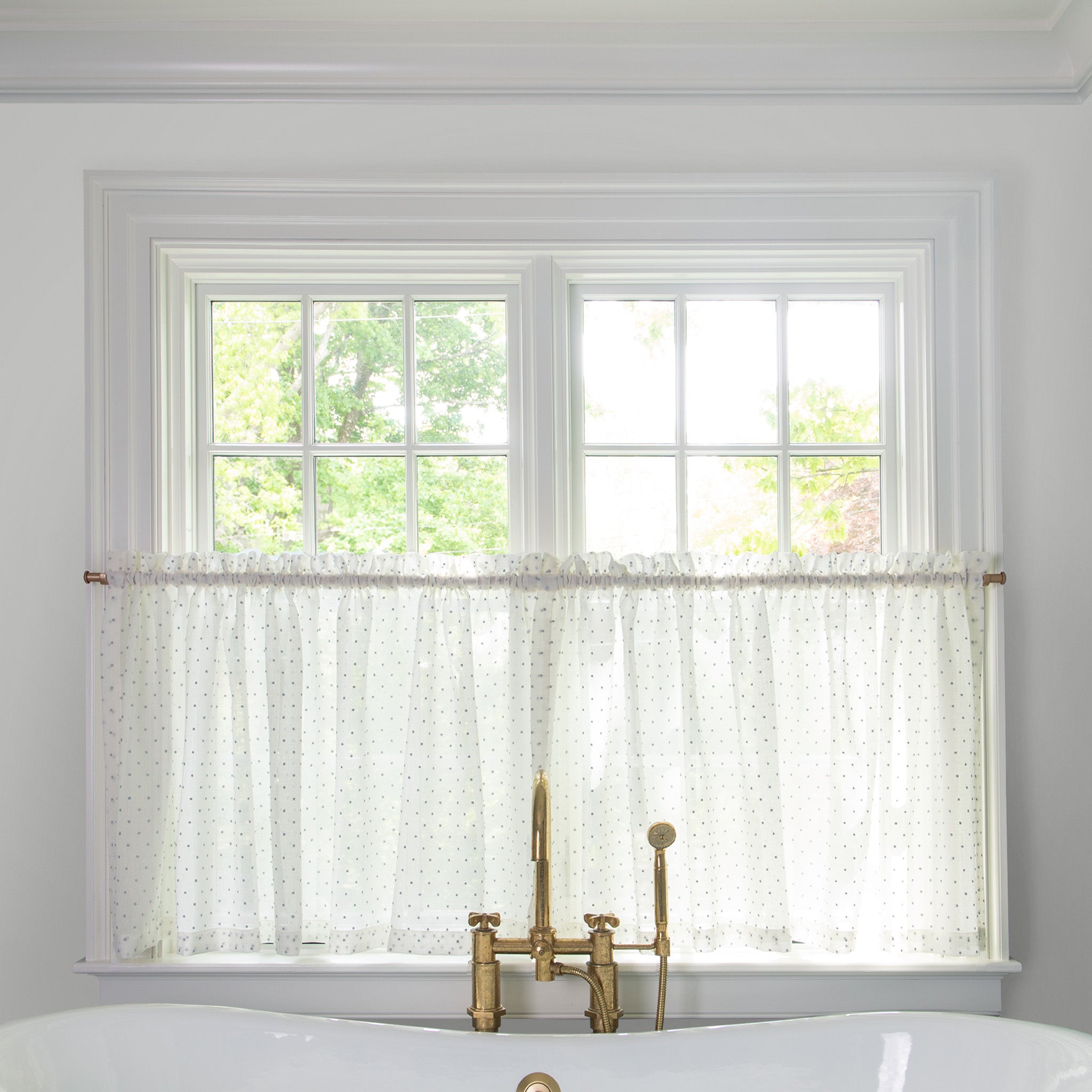 sheer white curtain embroidered with sky blue polka dots on a metal rod in front of an illuminated window in a bathroom