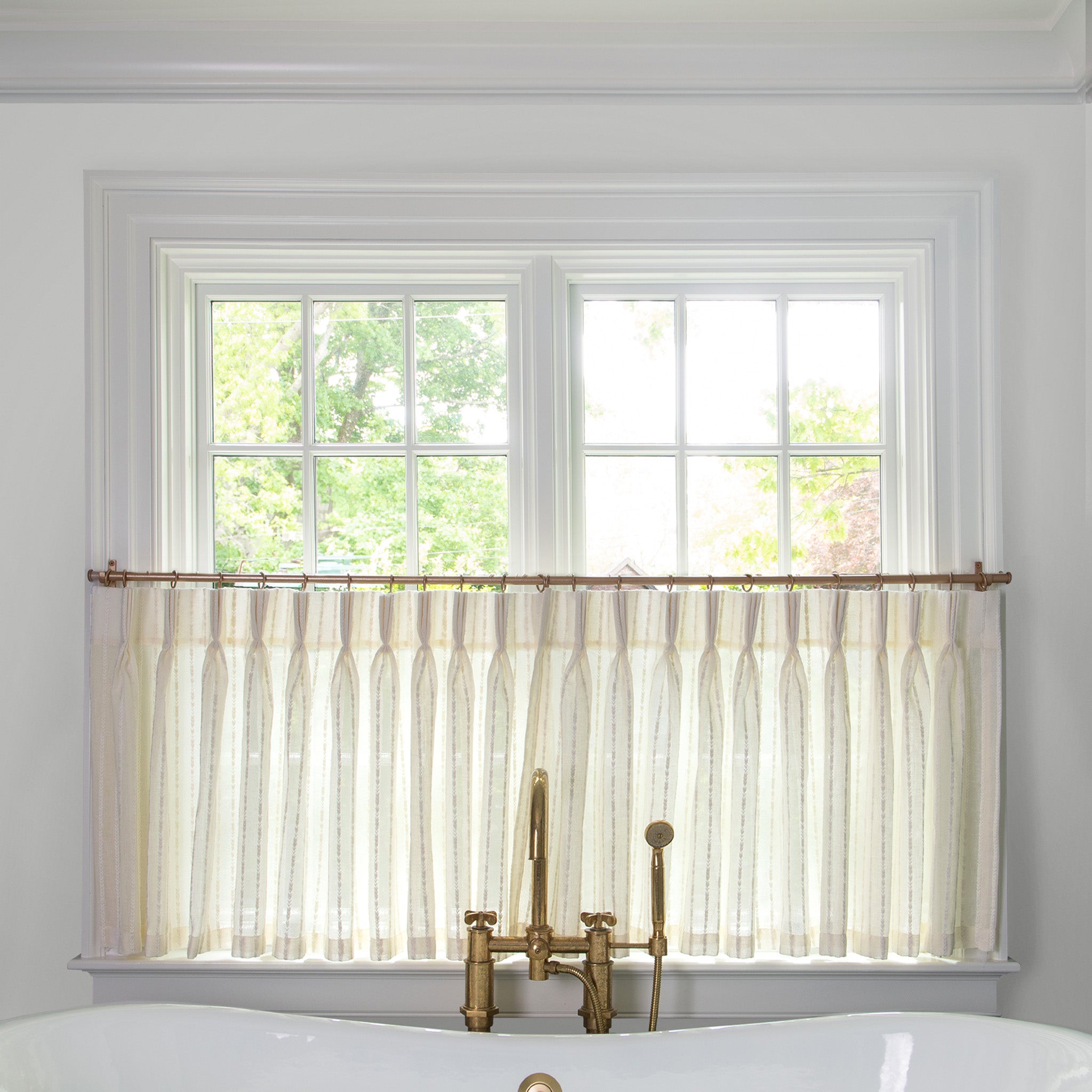 natural white curtain with neutral stripe pattern on a metal rod in front of an illuminated window in a bathroom 