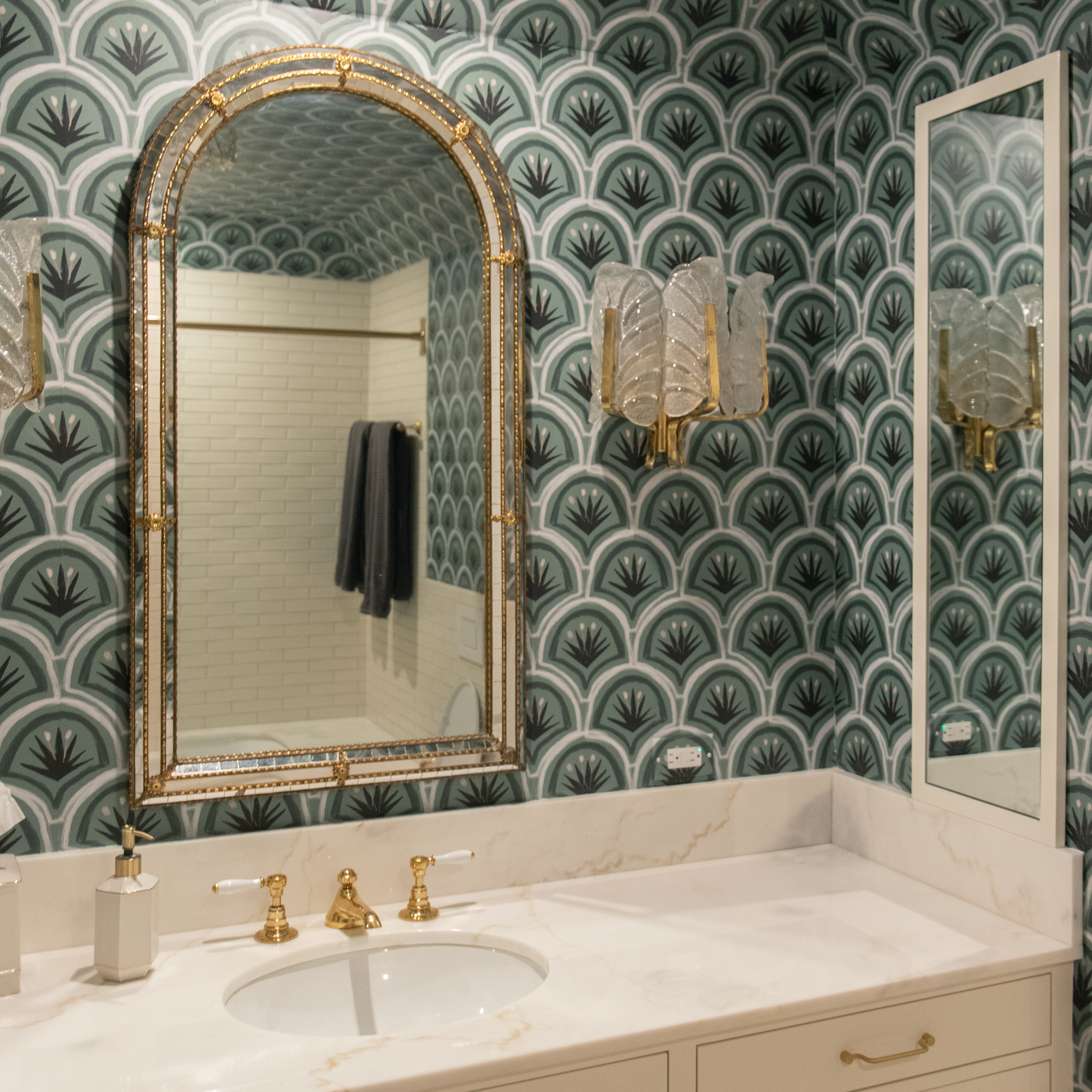 green art deco wallpaper in a bathroom with a white marble countertop with gold accents 