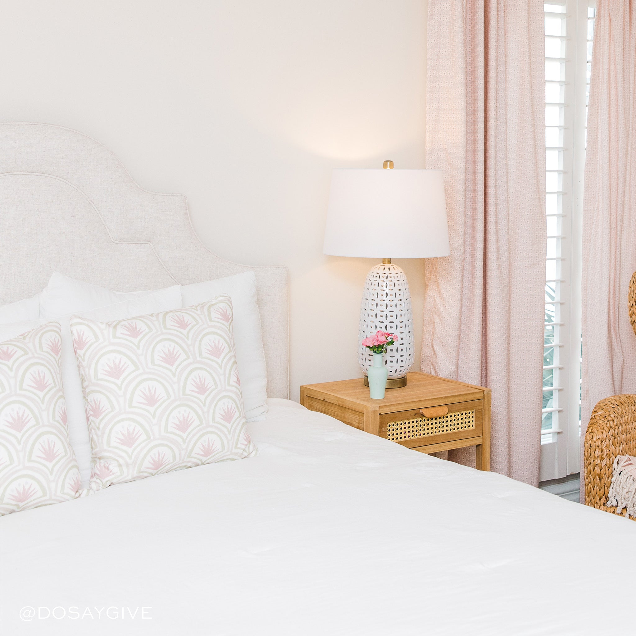 White bed close-up styled with two Pink Art Deco Palm Printed Pillows next to wooden nightstand with white lamp and flowers in vase on top next to Pink Geometric Printed Curtains