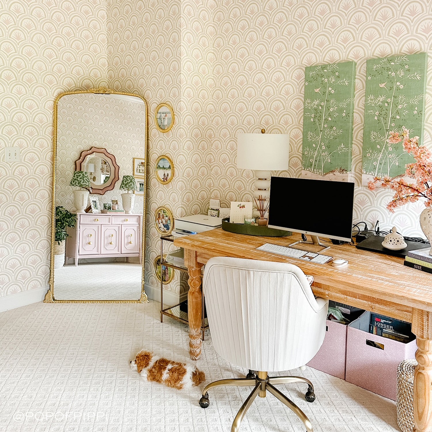 Office space styled with a Pink Art Deco Palm Printed Wallpaper next to wooden desk with white chair and dog laying on floor next to gold mirror reclining on wall. Photo taken by Pop Of Pippi