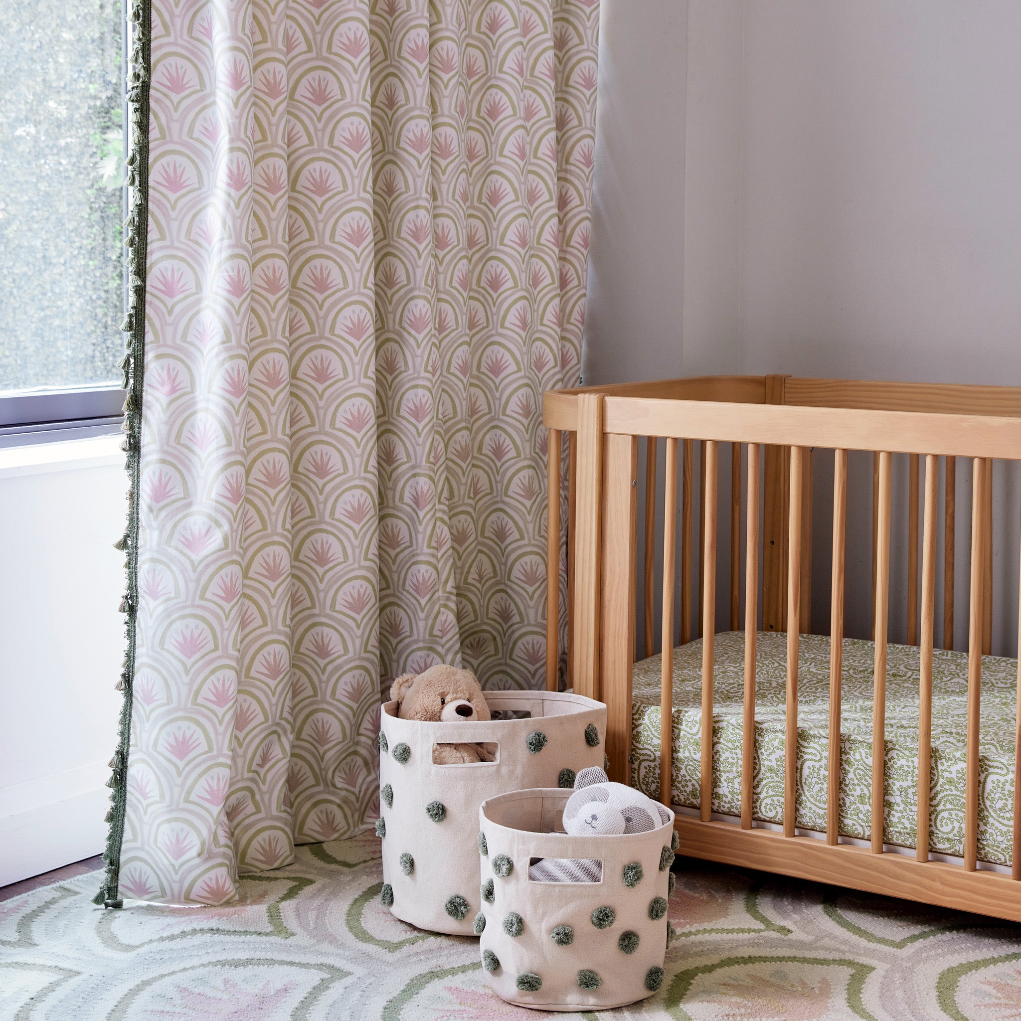 Nursery room corner styled with Pink Art Deco Palm Printed Curtains next to wooden crib and two baskets on floor with teddy bears in them over a Pink Art Deco Palm Printed Rug