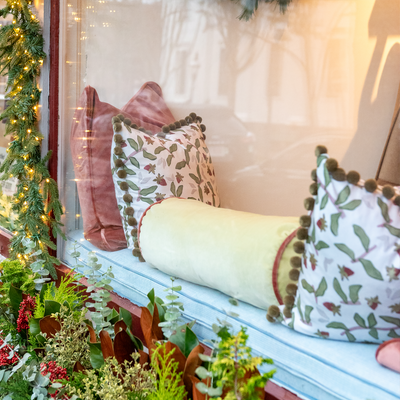 light green bolster pillow in a window in between two Strawberry & Botanical print pillows