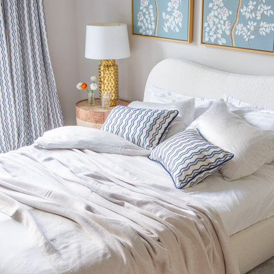 neutral background with blue wavy stripe pattern fabric pillows on a bed with white bedding  and as a curtain 
