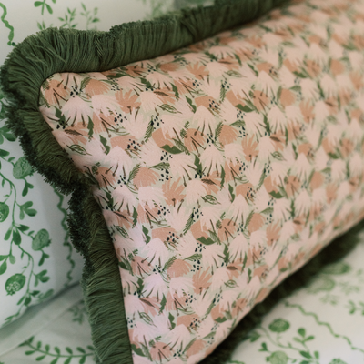Pink Floral pillow on a bed with sage green fringe trim 