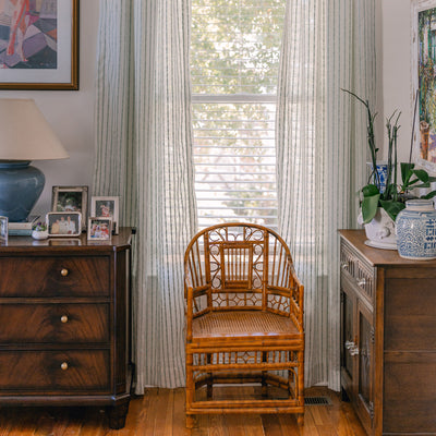 sheer white embroidered mint green stripe curtains hung in front of an illuminated window with a brown chair in front of the window and a brown dresser with family photos sitting on it and a blue lamp 