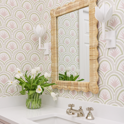 Pink Art Deco Palm wallpaper in a bathroom with white floral shaped light fixtures on either side of the mirror and a vase of white tulips sitting on a bathroom counter