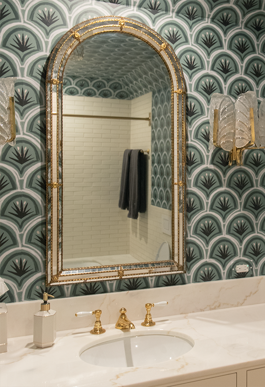 dark forest green art deco wallpaper in a bathroom with a mirror with gold trim on it and white marble counters