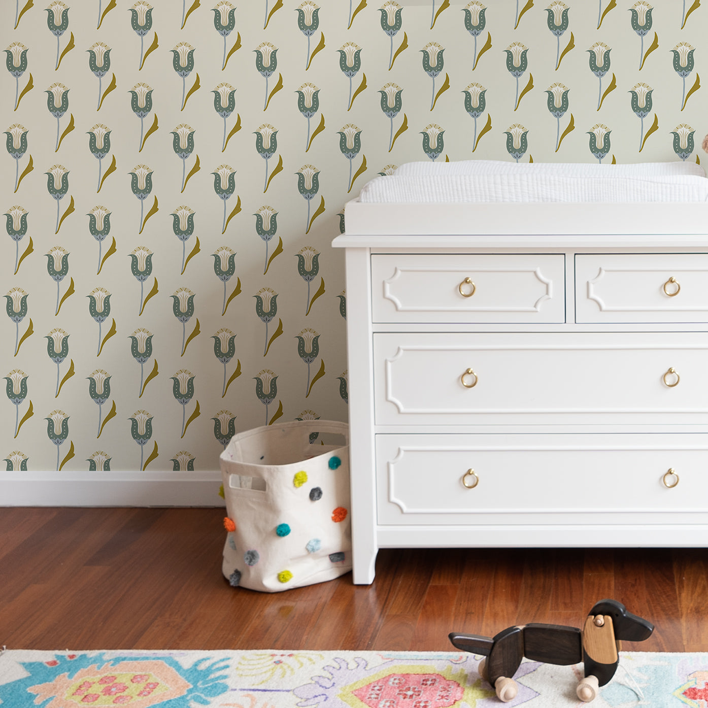 Abstract floral blue and green wallpaper on a wall with a white changing table with drawers in front with a colorful rug