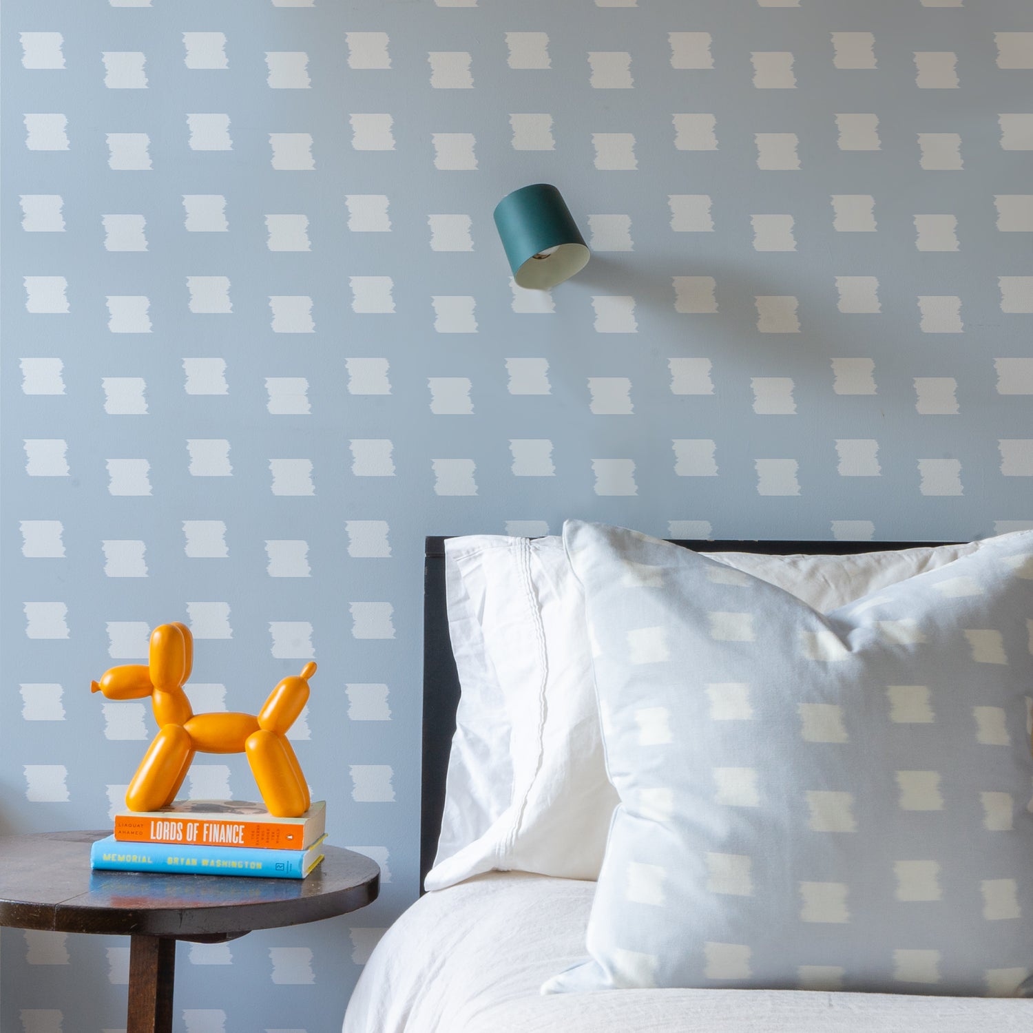 Bed Close-up styled with Sky Blue Pattern Printed Pillow on white bed next to wooden circular nightstand with two books stacked and orange decoration over Sky Blue Pattern Printed Wallpaper