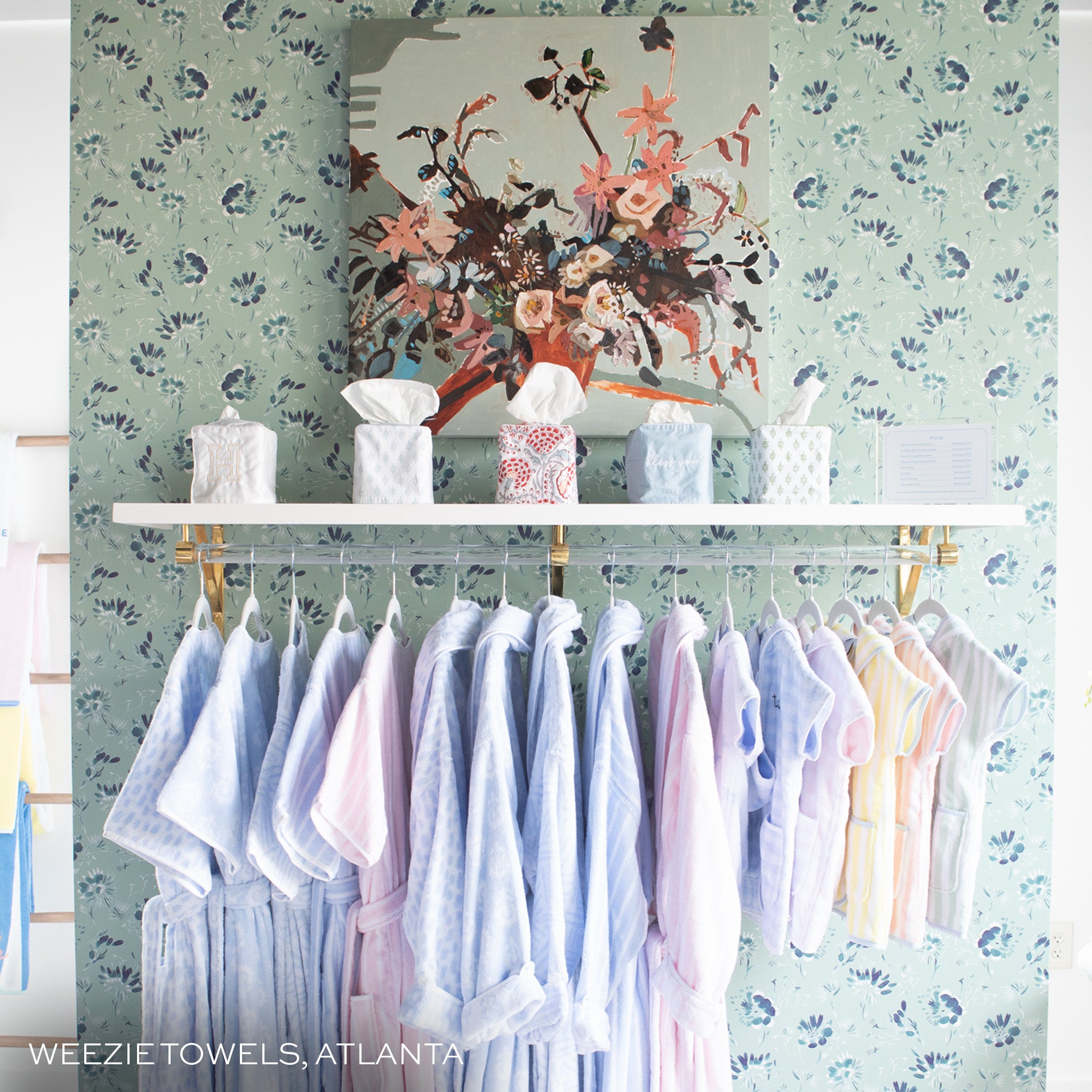 wall with blake mint clay coated wallpaper and a painting of flowers hung on the wall and a clothing rack with blue and pink clothes hung on it