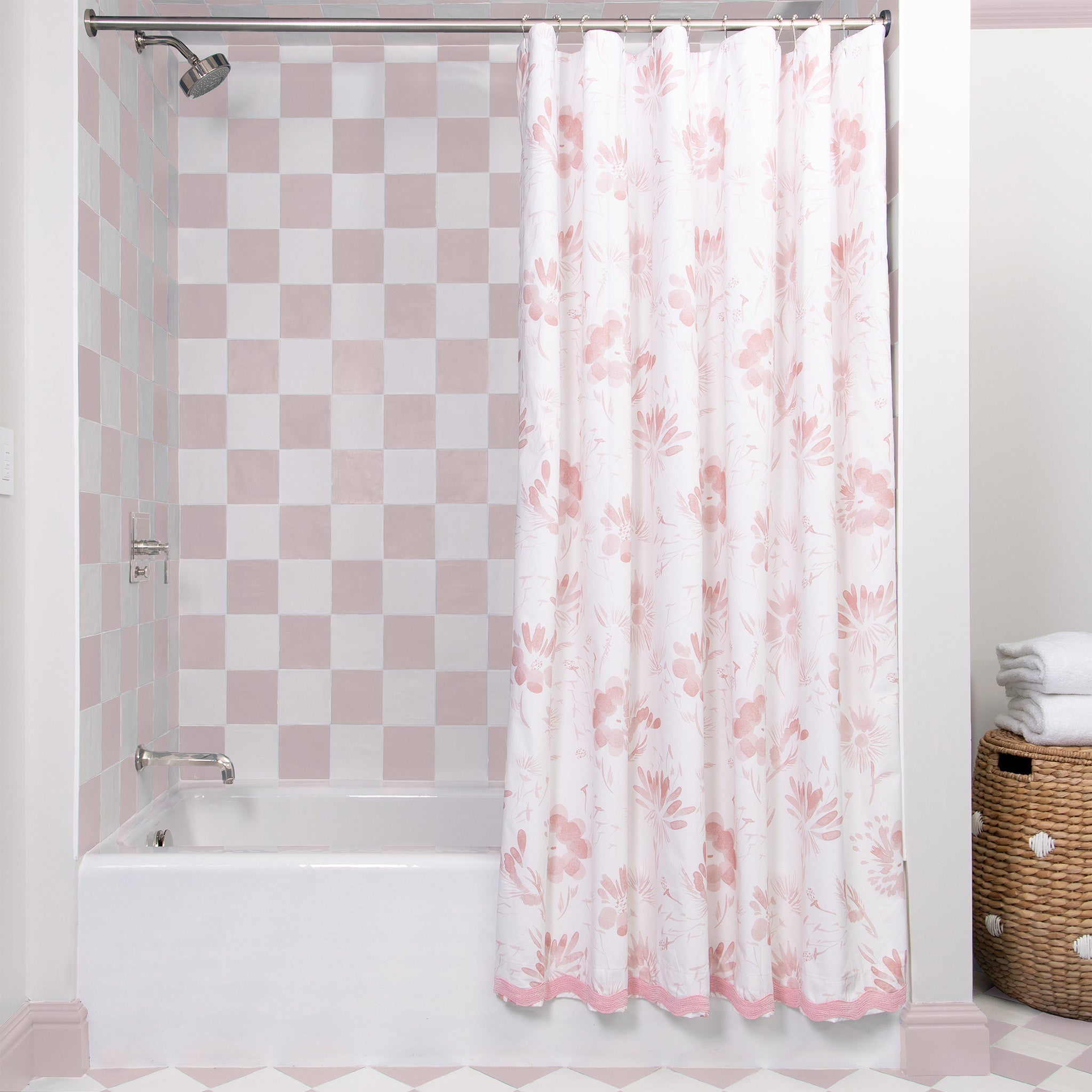 Pink Floral Shower curtain on metal rod with a pink and white checkered bath walls and laundry bin besides with two white towels on top