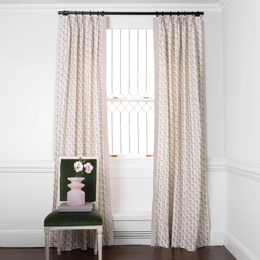 abstract floral pink and green patterned curtains on metal rod in front of an illuminated window with a green chair in front with flowers on it