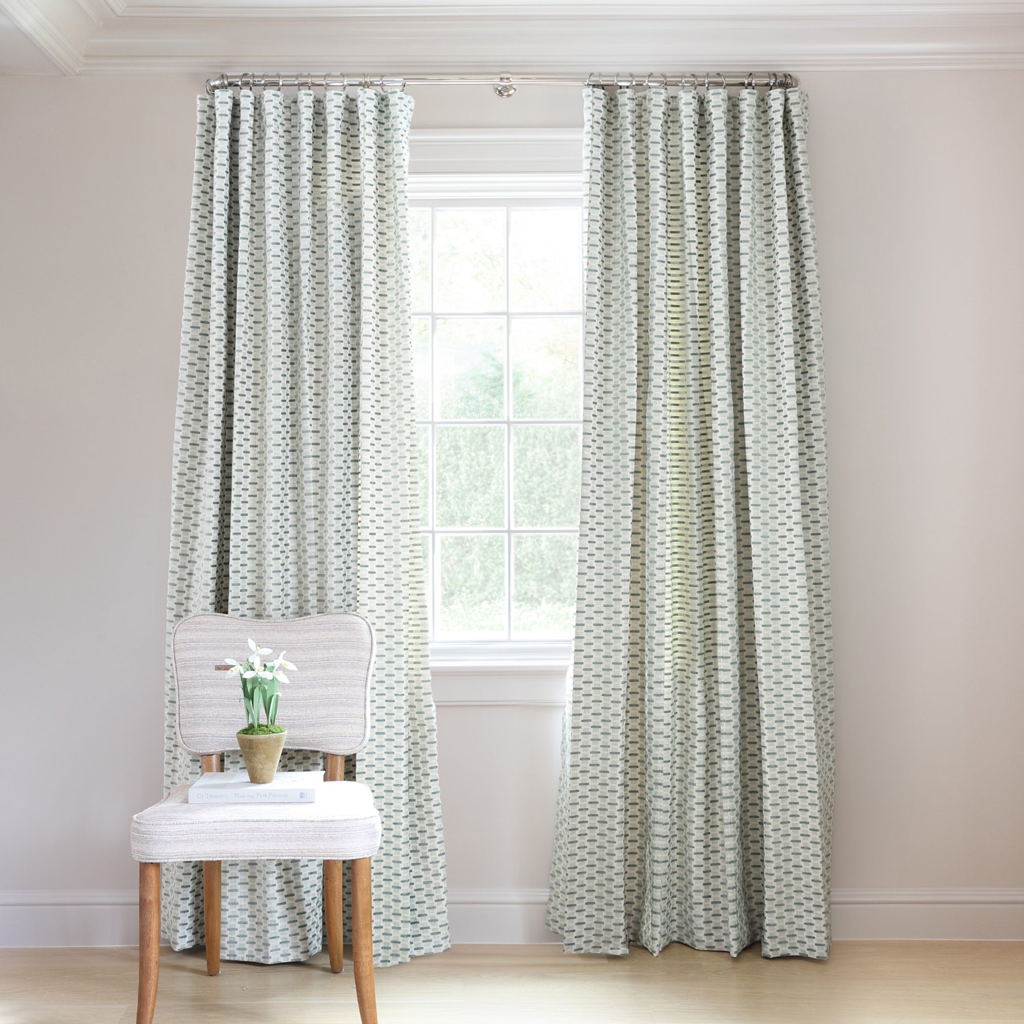 chenille and woven jacquard mint green geometric curtains on a metal rod in front of an illuminated window with a blue chair stacked with books