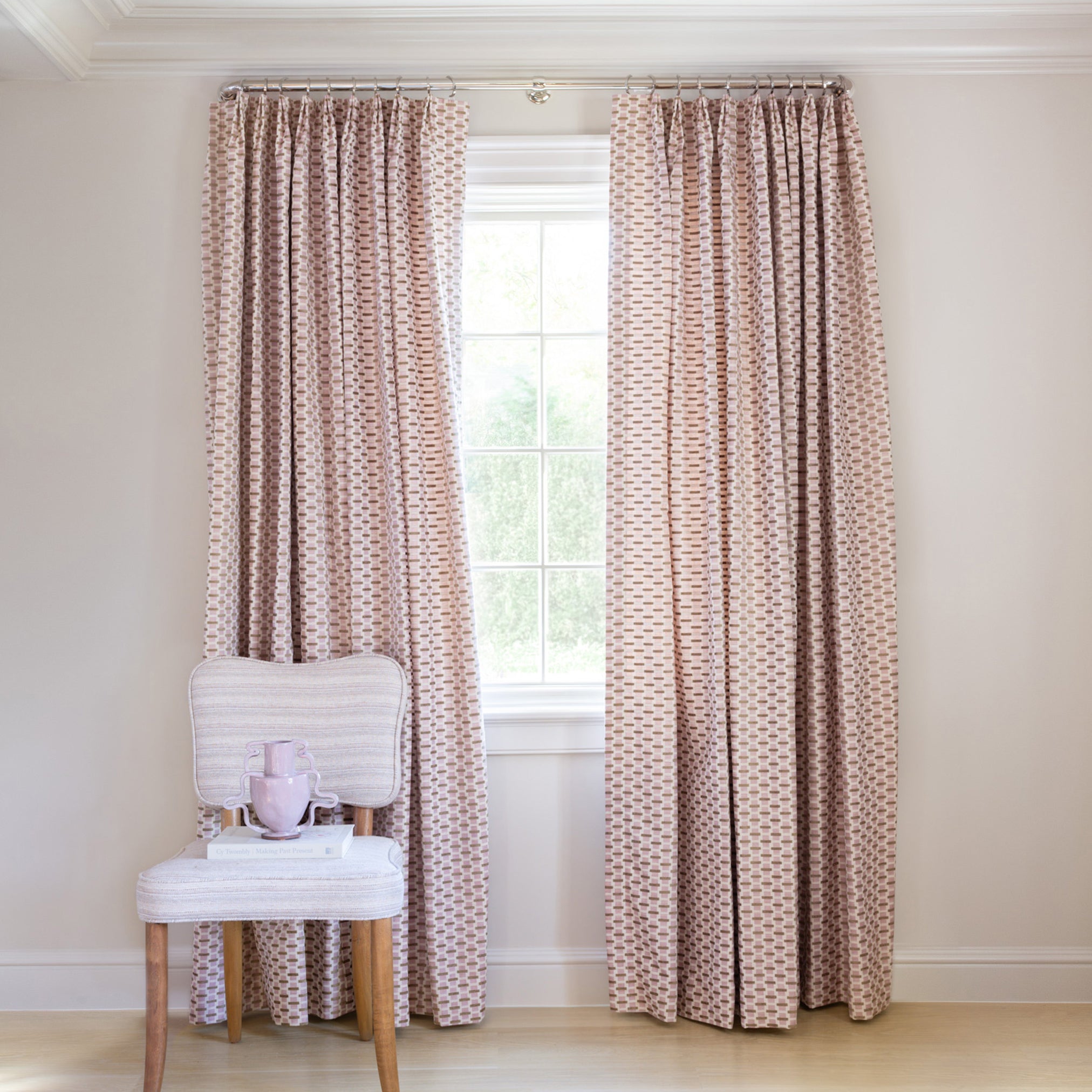  chenille and woven jacquard pink and citron geometric curtain on a metal rod in front of an illuminated window with a green chair stacked with books