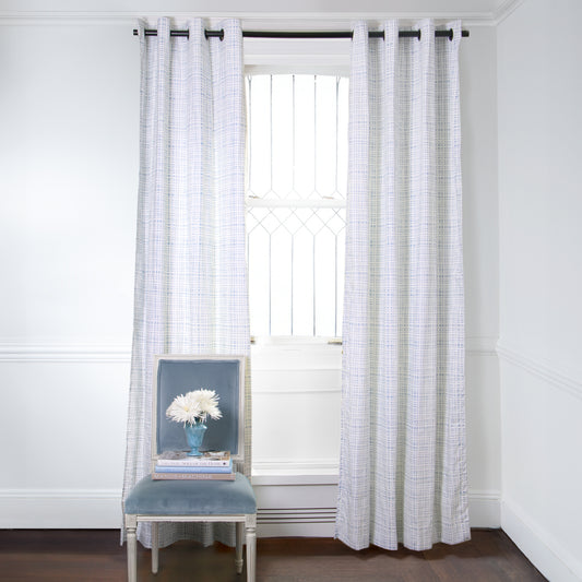 Sky Blue Gingham Printed Curtains on metal rod in front of an illuminated window with Blue Velvet chair with white flowers in blue vase on top of stacked books