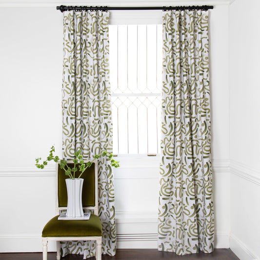 Moss Green Printed Curtains on white rod in front of an illuminated window with Green Velvet chair with white and plant in white vase on top of white book