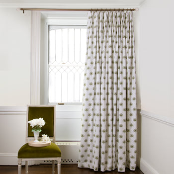 Green Floral Printed curtains on metal rod in front of an illuminated window with Green Moss chair with white flowers in white vase on top of plate