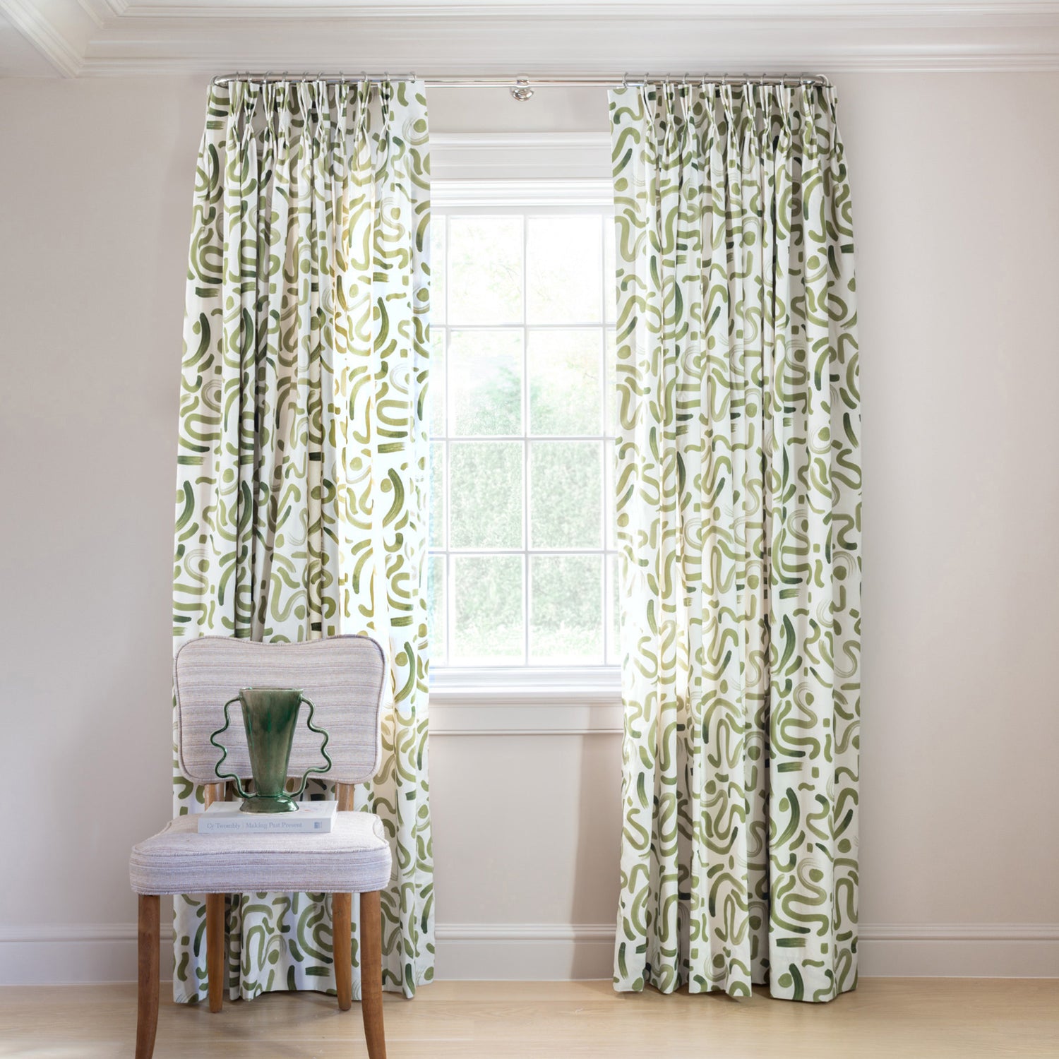 Moss Green Printed Curtains on white rod in front of an illuminated window with Green Velvet chair with white and plant in white vase on top of white book