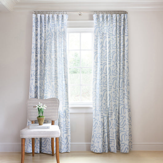 Hockney Sky Tailored Pleat curtains with custom hand-painted blue patterns brightening a sunlit window.