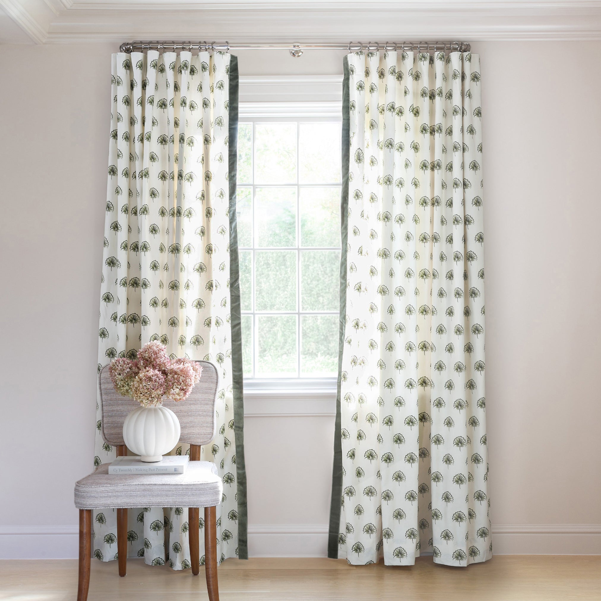 Green Floral Printed curtains on metal rod in front of an illuminated window with Green Moss chair with white flowers in white vase on top of plate