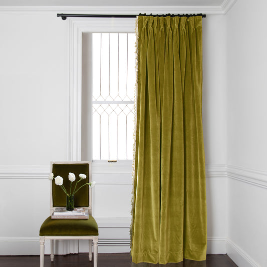 golden chartreuse curtains on a metal rod in front of an illuminated window with a dark green chair stacked with books
