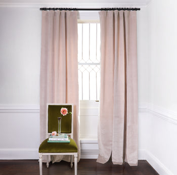 Pink Velvet Curtains on black rod in front of an illuminated window with Moss Green Velvet chair with flowers in clear vase on top of two stacked books