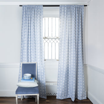 Sky Blue Pattern Printed Curtains on metal rod in front of an illuminated window with Sky Blue Velvet chair with bowl and stacked books on top of Pillow