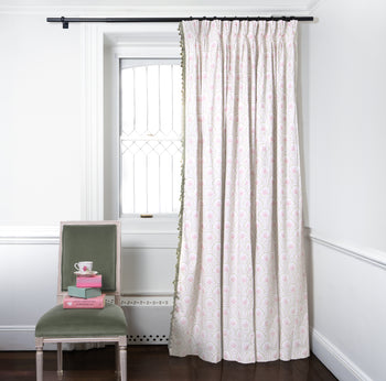 Pink Art Deco Palm Printed Curtains on metal rod in front of an illuminated window with Green Velvet chair with cup on top of stacked boxes