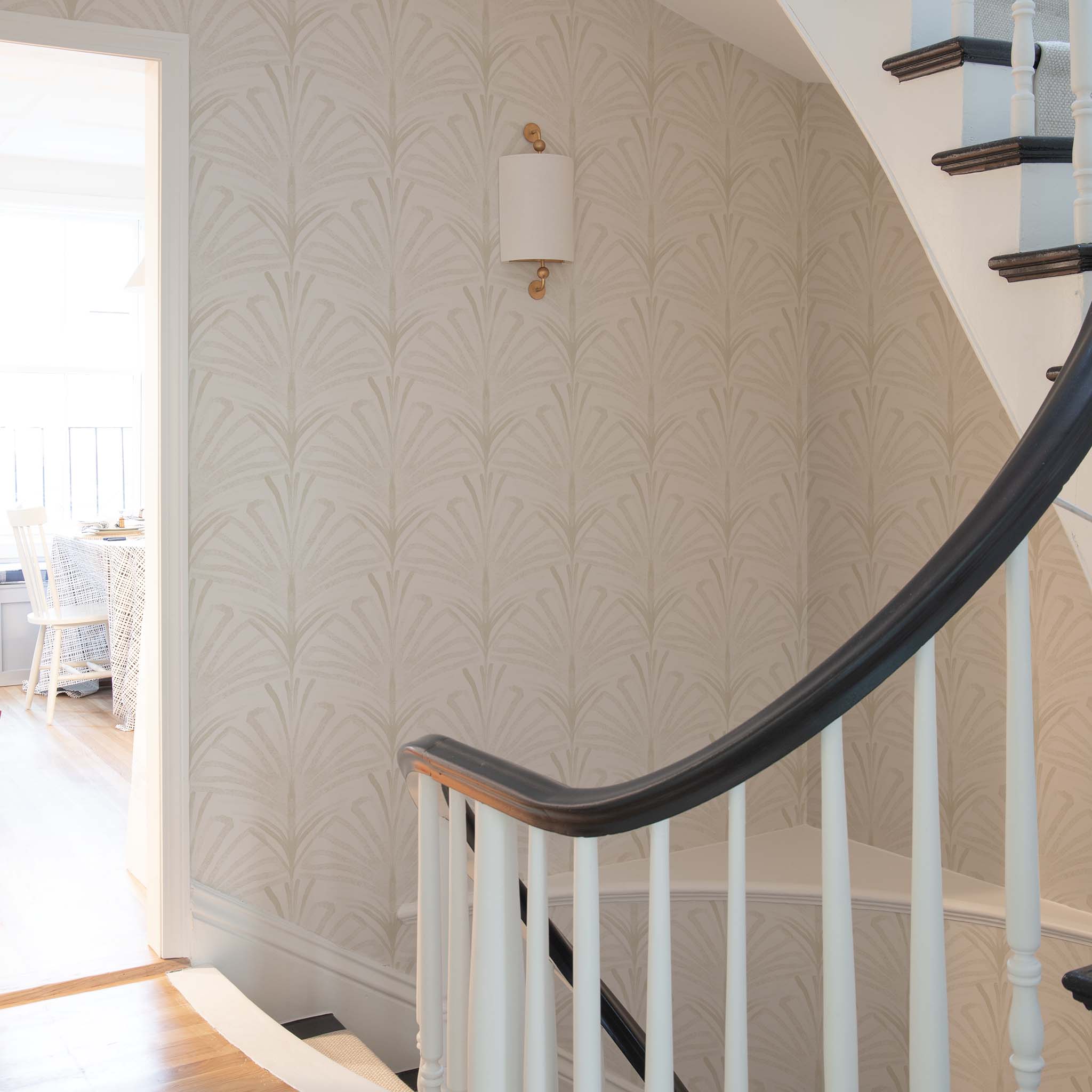 Curved staircase with white spindles and dark wooden handrail against neutral patterned wallpaper, showcasing made-to-order quality.