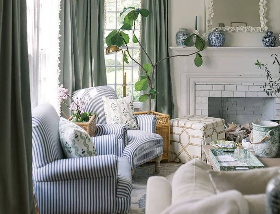 sage green curtains in a living room in front of illuminated windows with blue and white striped chairs and a white couch 