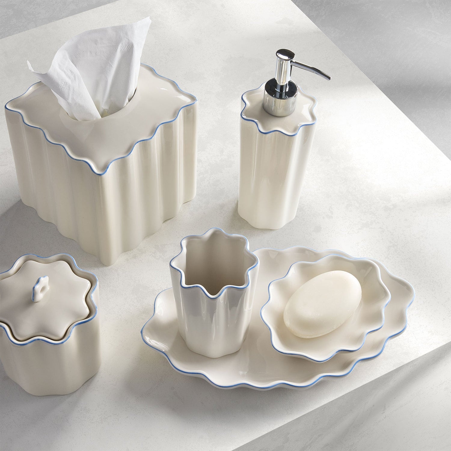 white ceramic tissue holder, cotton jar, lotion dispenser with silver pump, tumbler, and soap dish on top of a tray 
