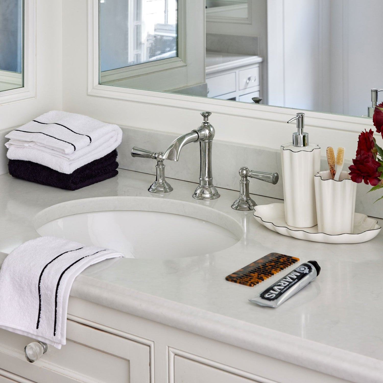 white ceramic lotion dispenser and tumbler on top of a white ceramic tray on a white marble bathroom counter next to a sink 