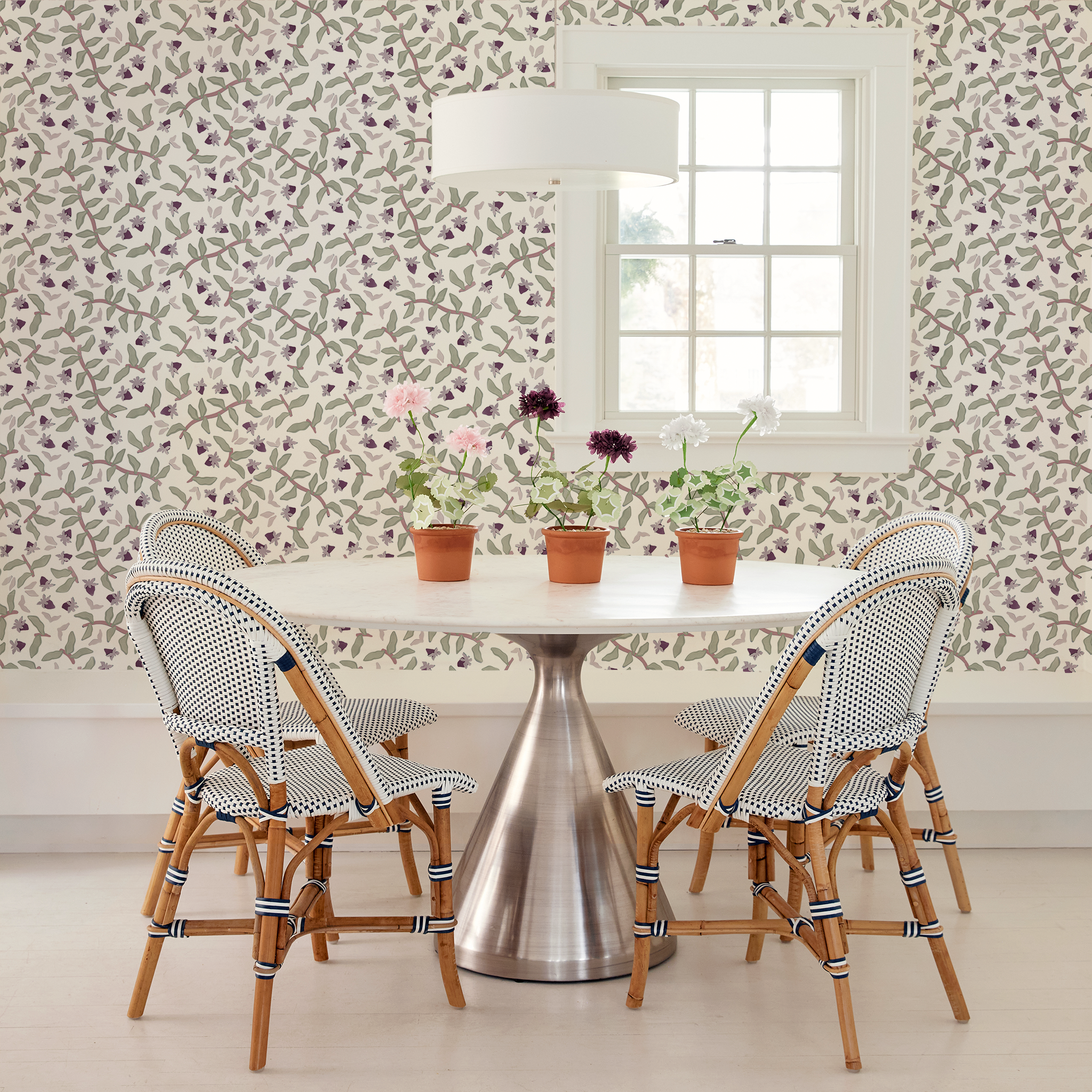 Round white table styled with three flower clay pots and four wooden chairs around next to Strawberry & Botanical Printed Wallpaper by small rectangular window