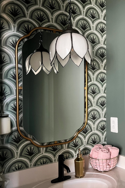 forest green and black art deco palm print wallpaper on a wall in a bathroom with a gold trim mirror on the wall and a white floral shaped light fixture hanging in front of the mirror 