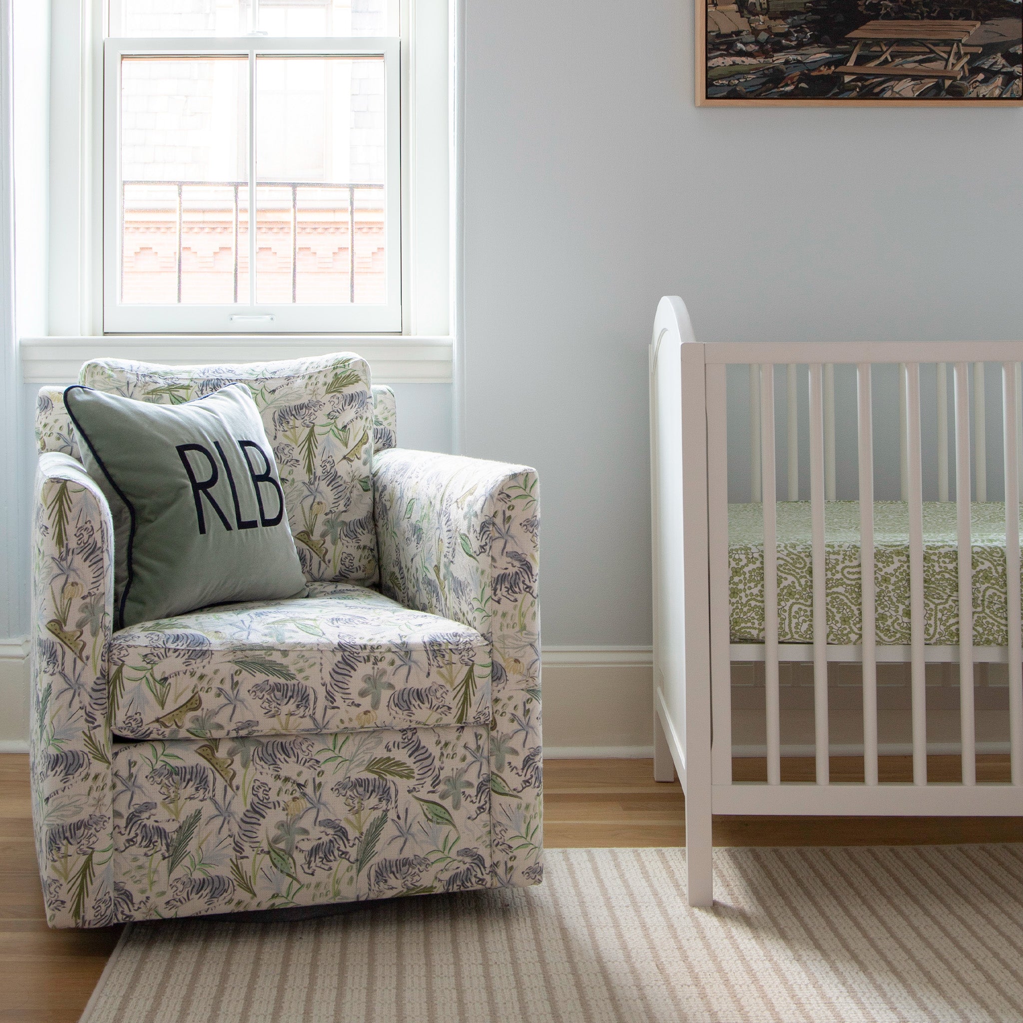 Nursery room with Green Tiger Printed Sofa Chair styled with a Blue Green Velvet Pillow next to white crib and illuminated window