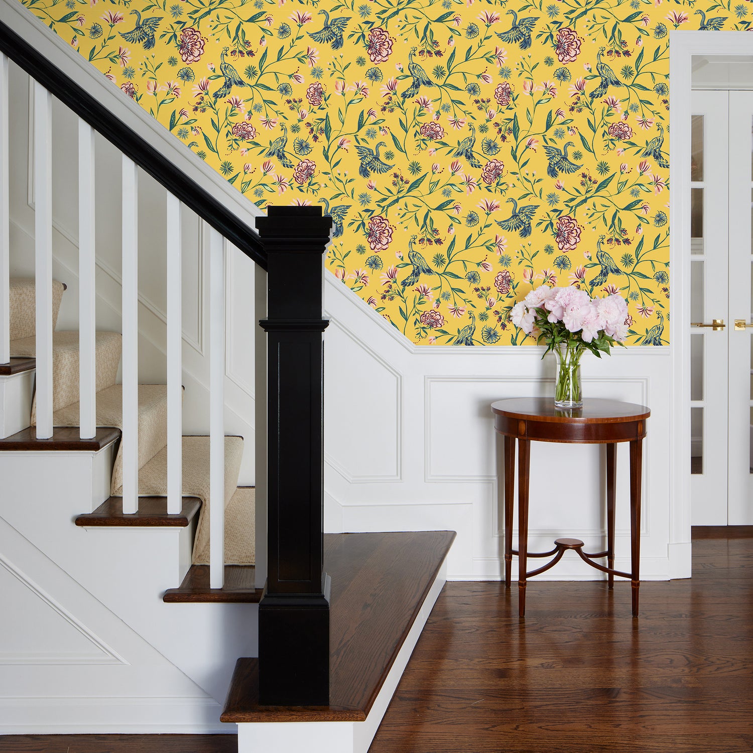 Stairs styled with Yellow Canary printed wallpaper and wooden small table in front with vase full of pink flowers on top