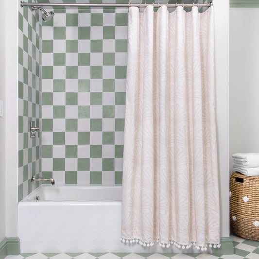 Beige Palm printed shower curtain hanging on rod in front of white tub in bathroom with green and white tiles