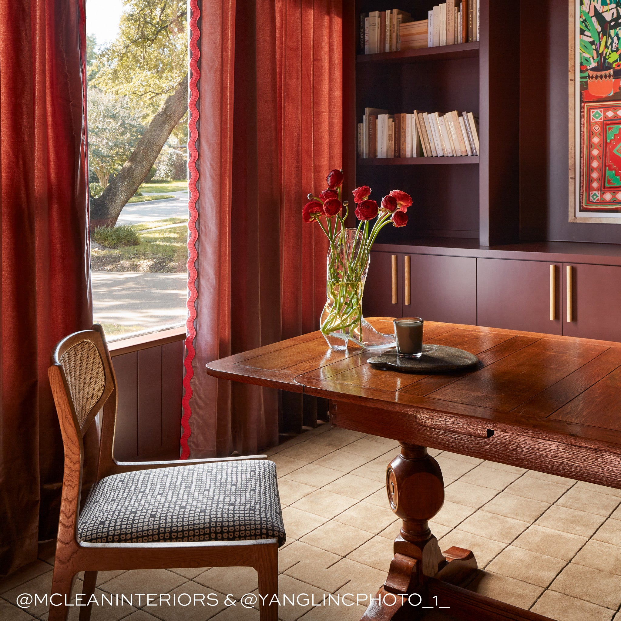 brown velvet curtains in front of a window with red trim and a brown wood desk and chair with a vase of flowers on the desk